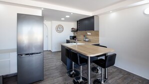 A modern kitchen with a stainless steel refrigerator, a wooden island with bar stools, and a built-in oven. - ZEN Apartment T2 "Waterfront" Baie Nettle (BAIE NETTLE)