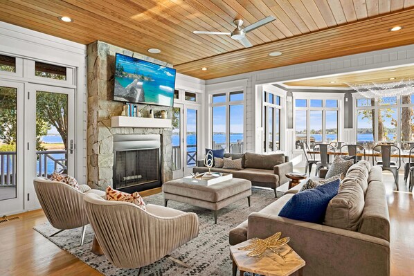 A spacious living room with a fireplace, comfortable seating, and large windows overlooking a scenic view. - VRBO Home of the Year | Heated Pool, Game Room, Putting Green, Peloton | Sleeps 18 | The Chasestone (Mooresville)