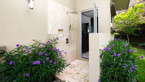 Un baño moderno con ducha, paredes de azulejos y un pequeño jardín con flores moradas.