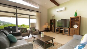 Un salón amplio con un televisor grande, asientos cómodos y vistas a espacios verdes.