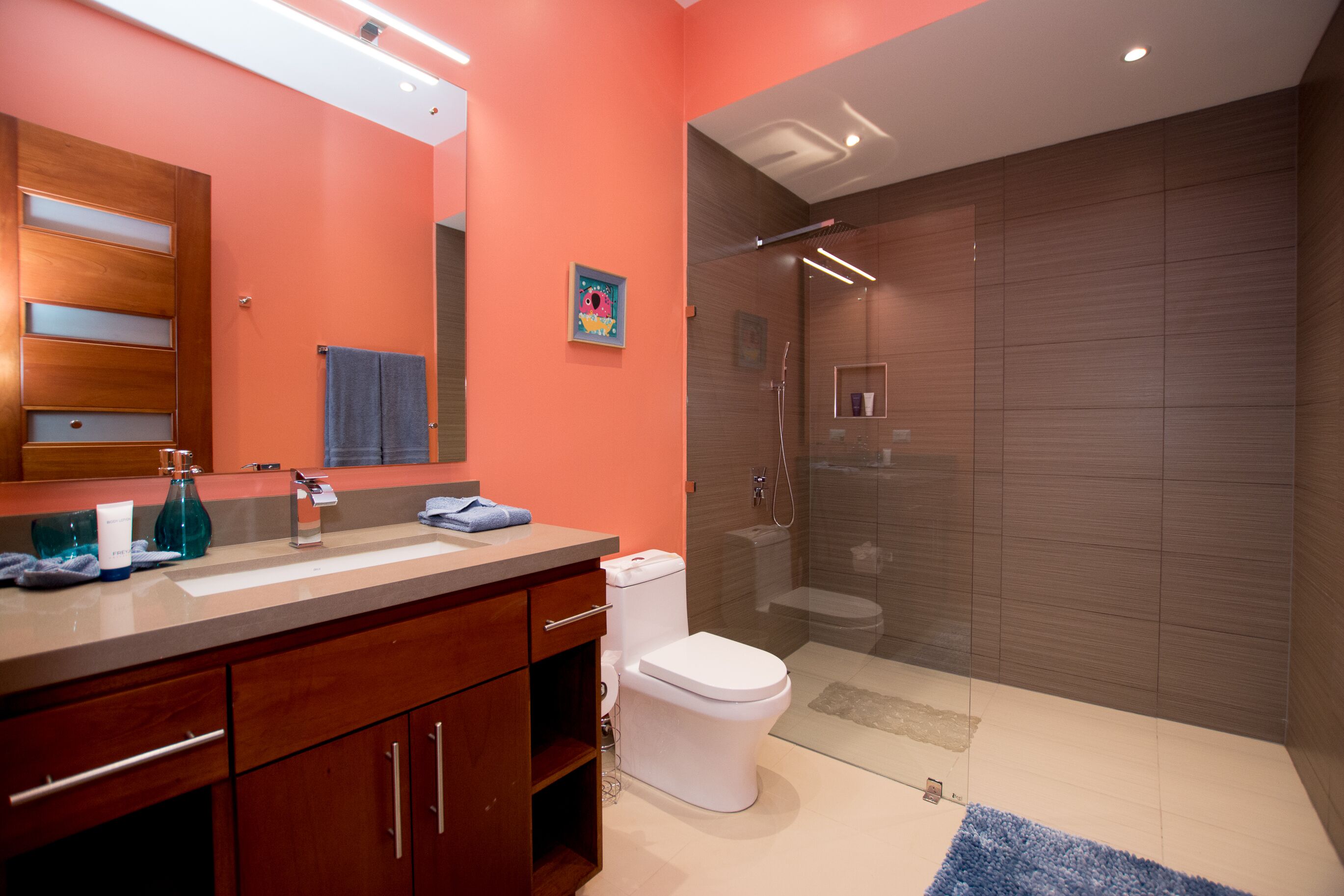 A modern bathroom with a wooden vanity, a white toilet, a glass-enclosed shower, and a large mirror.
