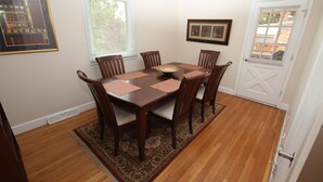 A dining room with a wooden table and chairs, a window with blinds, and a door with a view of the outside.