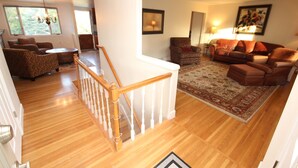 A spacious living area with a wooden staircase, a large rug, and multiple seating options including a sofa and chairs.