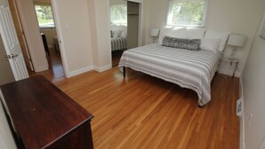 A bedroom with a large bed, wooden flooring, a closet, and a door leading to another room.
