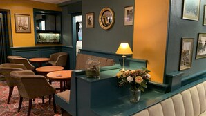 A reception area with a blue counter, a lamp, a vase with flowers, framed pictures on the wall, and a patterned carpet. - The Waverley Hotel (Whitehaven)