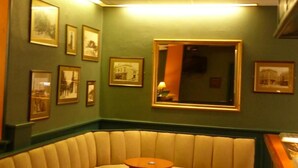 A corner seating area with a cushioned bench and round tables, framed pictures on the walls, and a patterned carpet. - The Waverley Hotel (Whitehaven)
