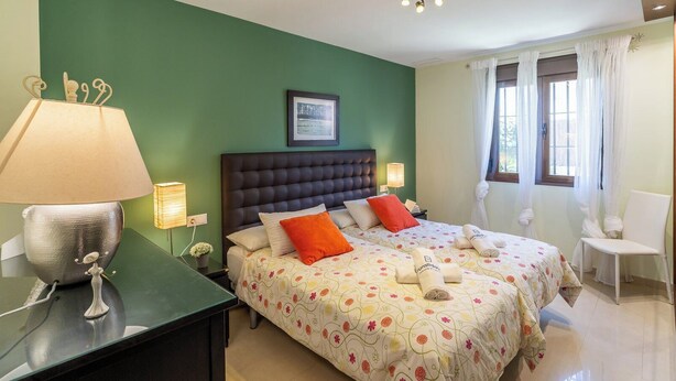 Una habitación de hotel con dos camas, una pared verde, un cuadro enmarcado y una ventana con cortinas.