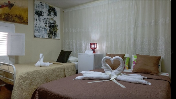 Une chambre d’hôtel avec deux lits, l’un décoré de serviettes en forme de cœur et l’autre de serviettes en forme de cygne. La chambre est également équipée d’un petit réfrigérateur et d’une table de chevet avec une lampe.