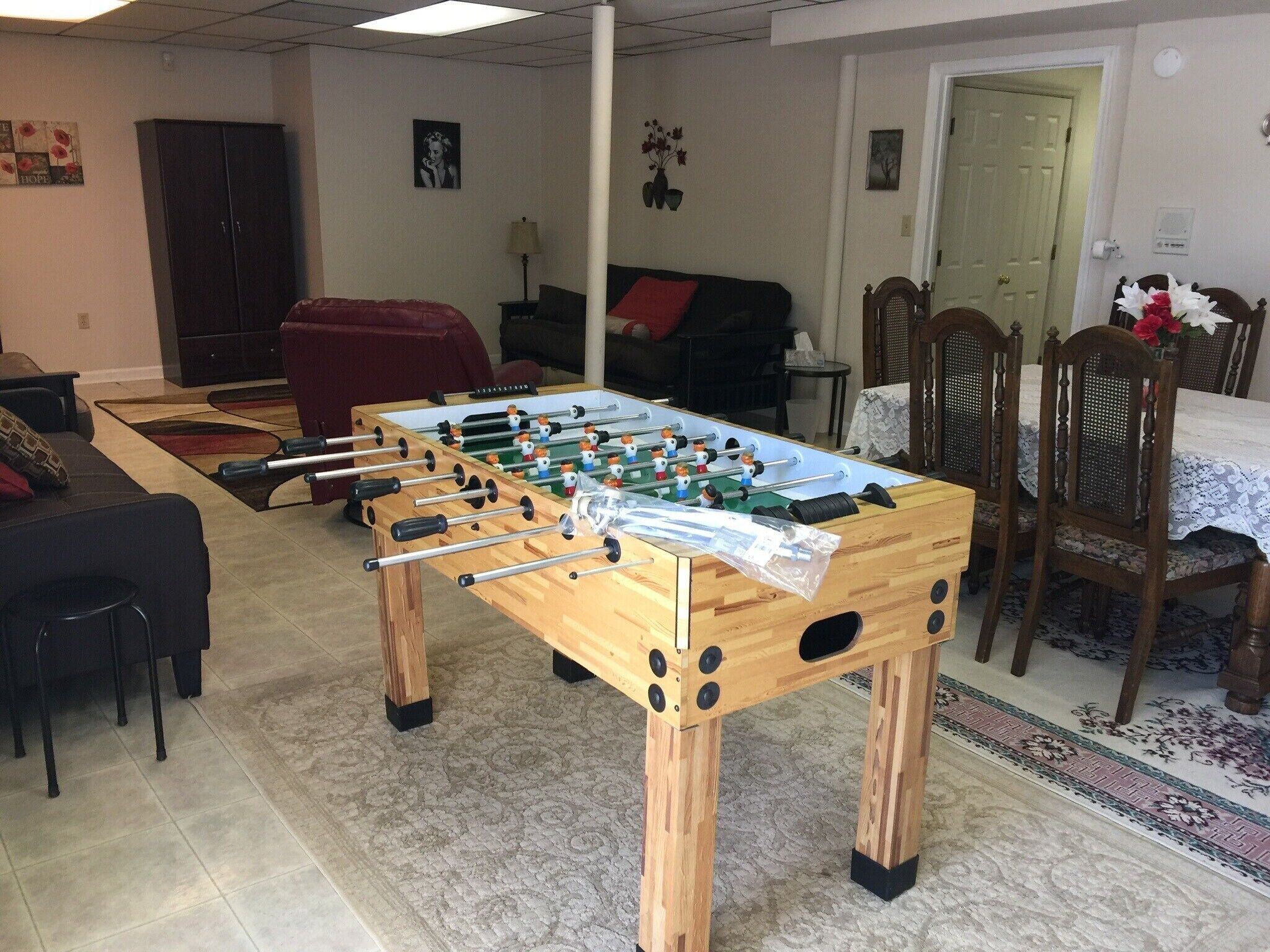 A room with a foosball table, a sofa, a dining table with chairs, and a cabinet.