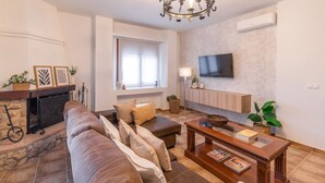 A living room with a fireplace, a sofa set, a wooden coffee table, and a television mounted on the wall. - Villa Las Gayumbas Villanueva de la Concepción by Ruralidays (Málaga)