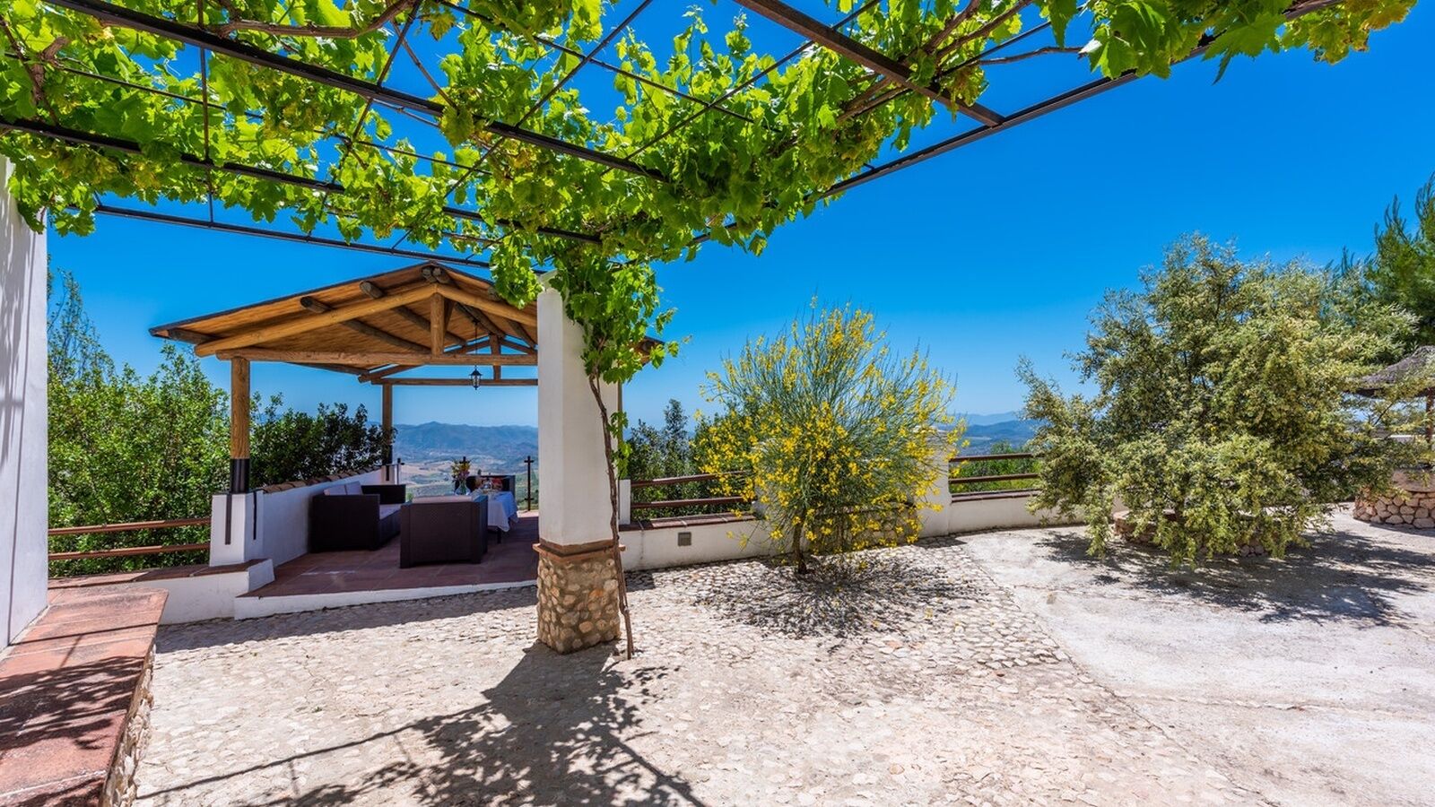Un patio al aire libre con pérgola, asientos y vistas del paisaje.
