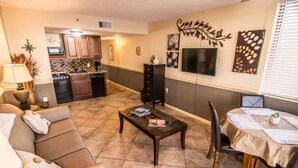 A living room with a sofa, coffee table, and dining area with a table and chairs. There is a kitchen in the background with cabinets and a stove. - 1101 Oceanfront End Unit Myrtle Beach HVAC UV SNAITIZER Lots of light and incredible views!! (Myrtle Beach)