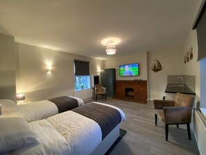 A modern hotel room with two beds, a TV, a fireplace, and a small seating area.