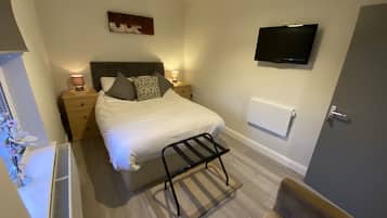 Quarto bem arrumado com cama, luminárias de cabeceira, televisão montada na parede e radiador.