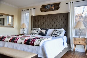 A bedroom with a large bed, a headboard, two bedside tables, and a window with curtains.