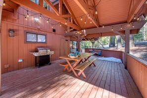 Enjoy al fresco dining on this outdoor deck with a wooden table and benches, barbecue grill, and string lights.