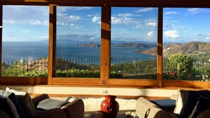 Quarto com uma grande janela com vista para a paisagem costeira, incluindo o mar e colinas ao longe.