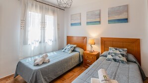 Une chambre d’hôtel avec deux lits, une tête de lit en bois, une table de chevet avec une lampe et une fenêtre avec des rideaux légers.