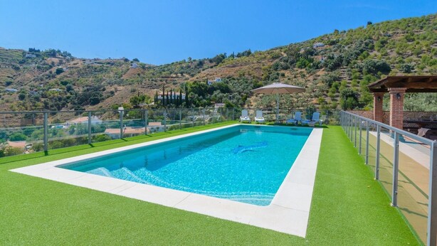 Une piscine rectangulaire à l’eau d’un bleu limpide, entourée de gazon artificiel vert et délimitée par une clôture métallique.