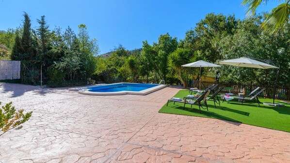 A swimming pool with a stone patio, surrounded by greenery and a fenced area. - El Molinillo Casabermeja by Ruralidays (Málaga)