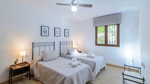 A bedroom with two beds, a ceiling fan, and a window with blinds. - El Molinillo Casabermeja by Ruralidays (Málaga)