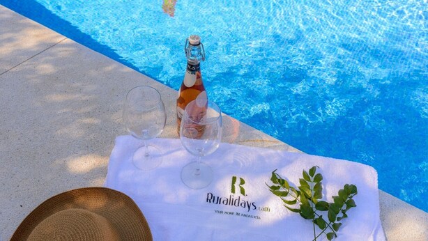 A poolside setting with a bottle of wine, two glasses, and a towel with a logo. - El Molinillo Casabermeja by Ruralidays (Málaga)