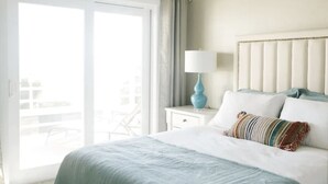A hotel room with a large bed, a nightstand with a lamp, and a view through a sliding door to an outdoor area. - Spinnaker Point Dr - Unbeatable BEACH FRONT property for a large group! (Garden City)