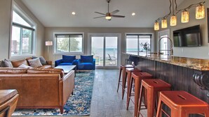 A spacious living area with a leather couch, blue armchairs, and a large window overlooking the ocean. - Spinnaker Point Dr - Unbeatable BEACH FRONT property for a large group! (Garden City)