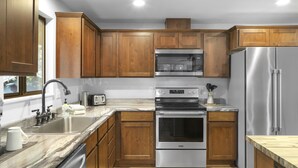 Una cocina moderna con armarios de madera, electrodomésticos de acero inoxidable, encimera de mármol y horno integrado.