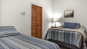 Un dormitorio con dos camas, una puerta de madera, una mesita de noche con una lámpara y un cuadro enmarcado en la pared.