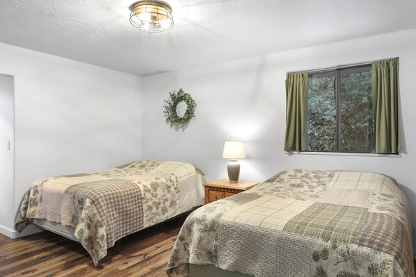 Une chambre avec deux lits, une table de chevet avec une lampe, une fenêtre avec des rideaux et une guirlande décorative accrochée au mur.
