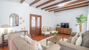 A living room with a sofa, armchairs, a coffee table, a TV, a wooden cabinet, and a plant. - Casa El Torero El Bosque by Ruralidays (Cádiz)