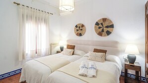 Un lit double avec une tête de lit, deux tables de chevet avec des lampes, une fenêtre avec des rideaux et deux éléments de décoration murale.