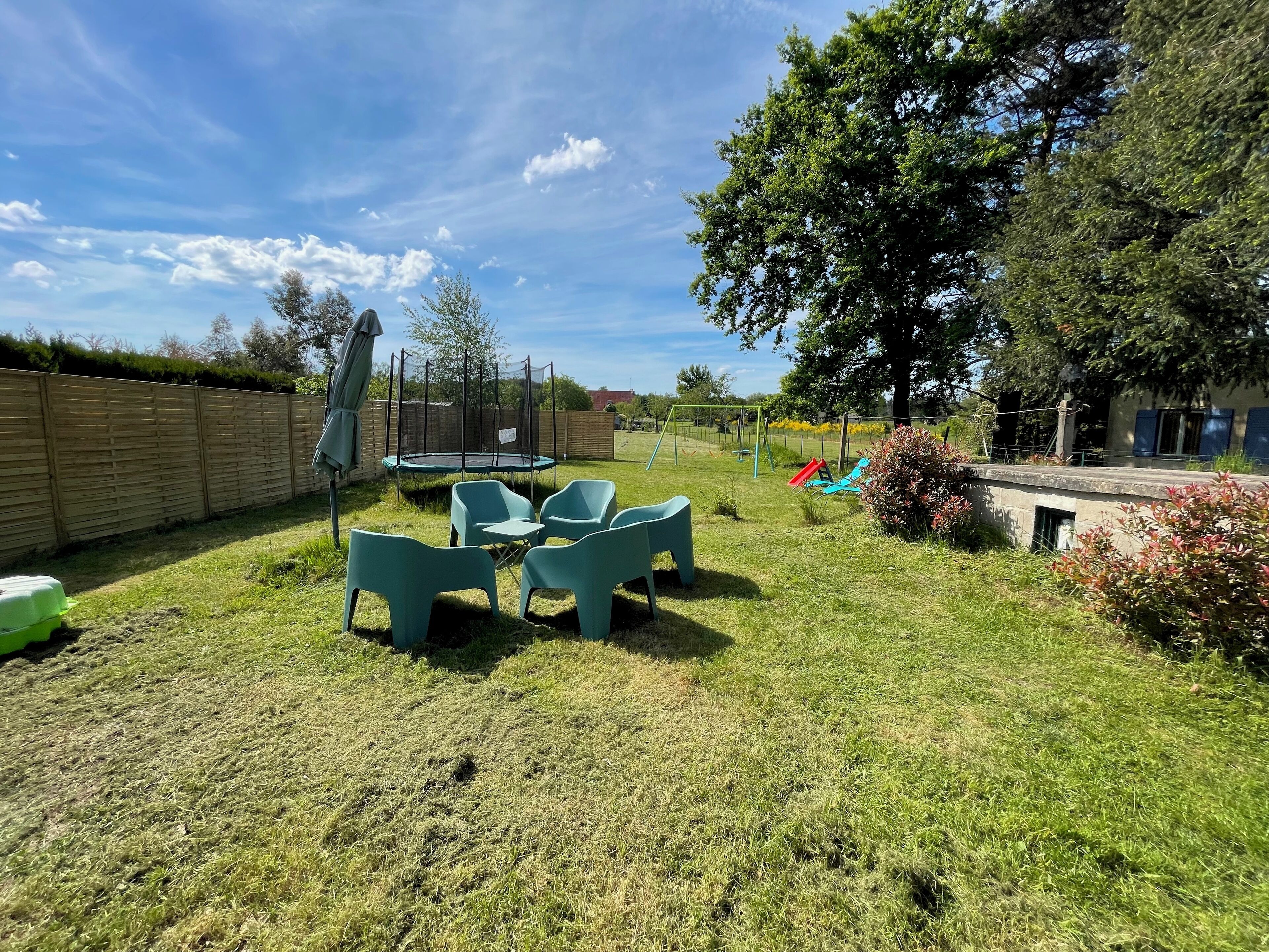 A backyard with a trampoline, green plastic chairs, and a swing set.