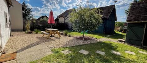A backyard with a picnic table and umbrella, surrounded by a gravel path and grass.