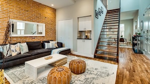 A modern living room with a brick wall, a staircase, and a kitchen area. - Stunning Home on Capitol Hill (Washington)