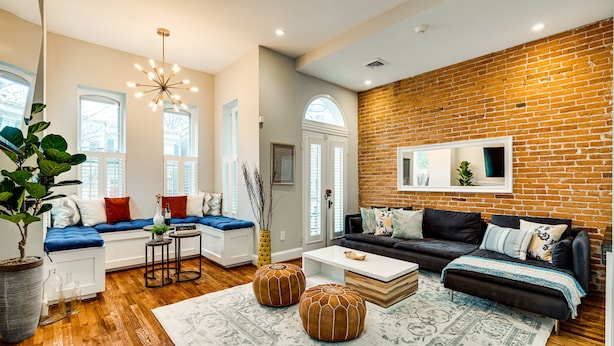 A modern living room with a brick wall, wooden flooring, and a mix of seating areas including a sofa and a bench. - Stunning Home on Capitol Hill (Washington)