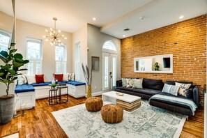 A modern living room with a brick wall, wooden flooring, and a mix of seating areas including a sofa and a bench. - Stunning Home on Capitol Hill (Washington)