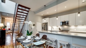 A modern kitchen with white cabinets, stainless steel appliances, and a glass dining table. - Stunning Home on Capitol Hill (Washington)