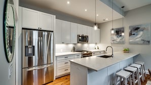 A modern kitchen with stainless steel appliances, white cabinetry, and a central island with bar stools. - Stunning Home on Capitol Hill (Washington)