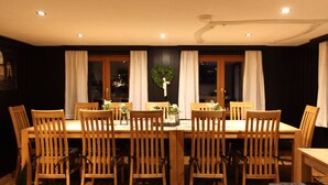 A dining room with a wooden table and chairs, a heart-shaped wreath on the wall, and a view of the city at night. - Chalet Mirandum Rustiko (Vandans)