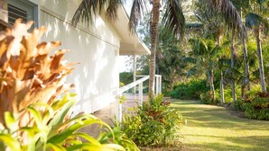 A white building with a covered porch, surrounded by lush greenery and palm trees.