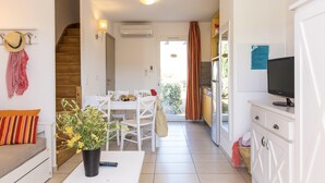 A modern living room with a sofa, a dining table, a TV, and a staircase leading to another room. - Maisonnette 10 Minutes de la Plage | Mini-Golf! (Belgodère)