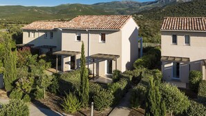 A modern two-story house with a tiled roof, surrounded by lush greenery and mountains in the background. - Maisonnette 10 Minutes de la Plage | Mini-Golf! (Belgodère)