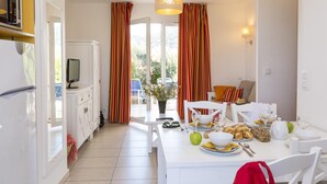 A modern kitchen with a dining area, white cabinets, a TV, and a table set for breakfast. - Maisonnette 10 Minutes de la Plage | Mini-Golf! (Belgodère)