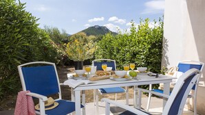 An outdoor dining area with a table set for breakfast, surrounded by chairs, and a view of a mountain. - Maisonnette 10 Minutes de la Plage | Mini-Golf! (Belgodère)
