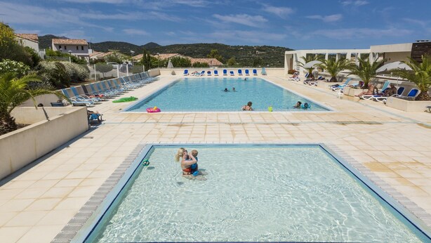 A swimming pool with lounge chairs and umbrellas, surrounded by buildings and hills. - Maisonnette 10 Minutes de la Plage | Mini-Golf! (Belgodère)
