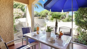 An outdoor patio with a table set for two, a blue umbrella, and a potted plant. - Maisonnette Chaleureux près de la Plage ! (Cap d'Agde)