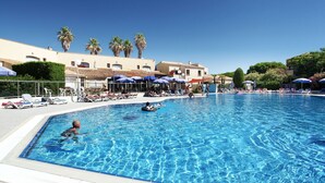 A swimming pool with lounge chairs and umbrellas, surrounded by buildings with palm trees. - Maisonnette Chaleureux près de la Plage ! (Cap d'Agde)