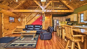 A log cabin interior with a wooden staircase, a living area with leather furniture, and a kitchen with wooden cabinets. - Ski Lodge Mtn Retreat w/ Fire Pit, Deck & Views! (Starksboro)